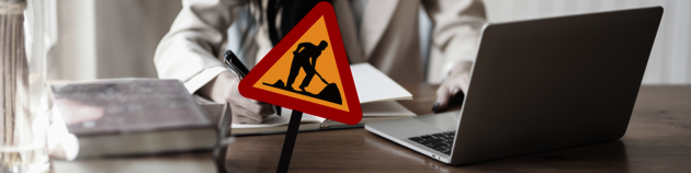 A photo of a person working on a computer behind a road works sign.