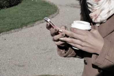 Two hands holding a mobile phone and a cup of coffee