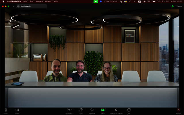 The three project members are seated behind a desk in a virtual office background. They are smiling at the camera.