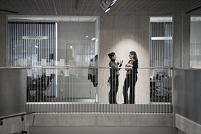 Two people are standing by a railing. They look at each other and seem to be having a conversation.