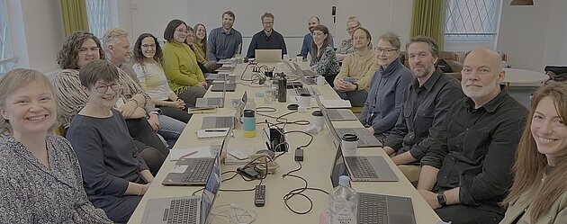 20 people seated around a table. Everyone is smiling and looking at the camera.