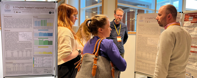 A group of people discussing in front of a poster. The poster itself is seen to the left of the phot of the people.